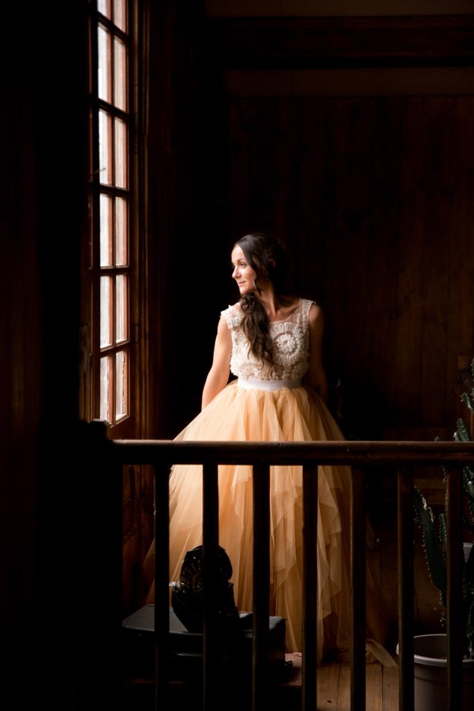 Mariée en robe élégante regardant par la fenêtre dans une ambiance chaleureuse