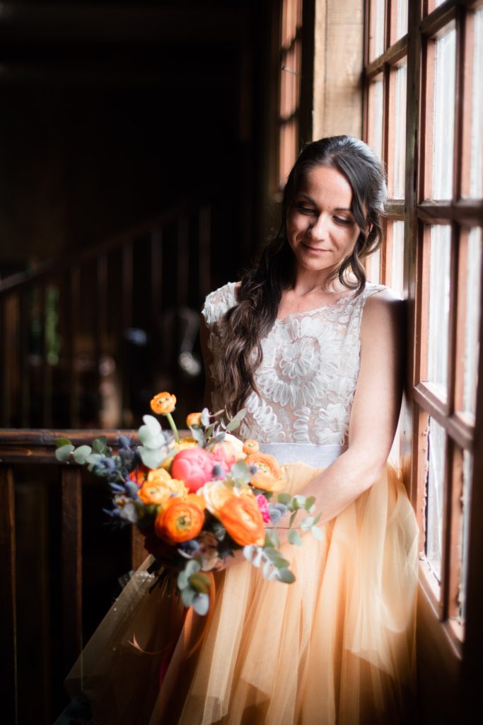 Mariée tenant un bouquet de fleurs colorées près d'une fenêtr