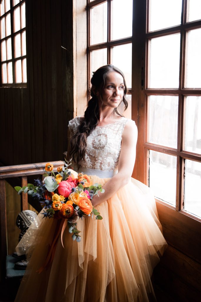 Mariée tenant un bouquet de fleurs colorées près d'une fenêtr