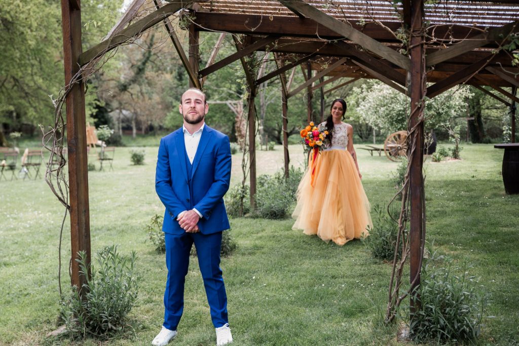 Marié en costume bleu attendant sous une pergola en bois pendant un first look mariage dans les Landes