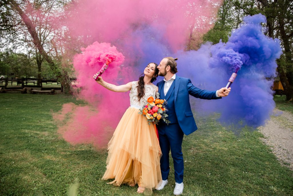 Mariés utilisant des fumigènes rose et bleu pour une séance photo originale de mariage