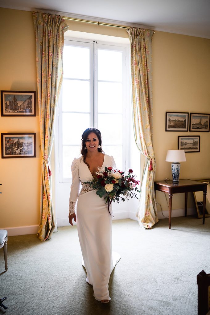 mariée avec bouquet devant fenêtre lumière naturelle mariage
