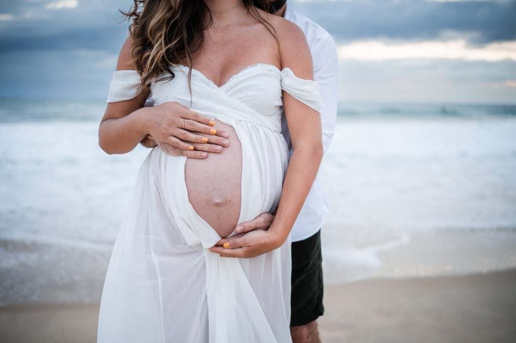 mains du couple sur le ventre de grossesse au bord de l’océan à Mimizan