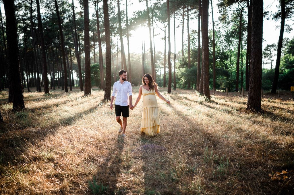 couple main dans la main dans la forêt lors d’une séance grossesse à Mimizan dans les Landes