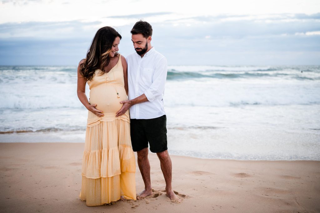 couple regardant le ventre de grossesse sur la plage pendant une séance photo à Mimizan