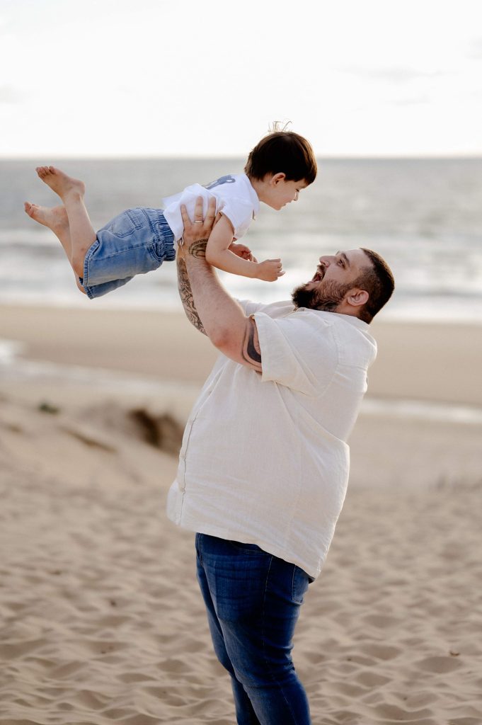 papa portant son bébé lors d’une séance photo famille à la plage à Mimizan