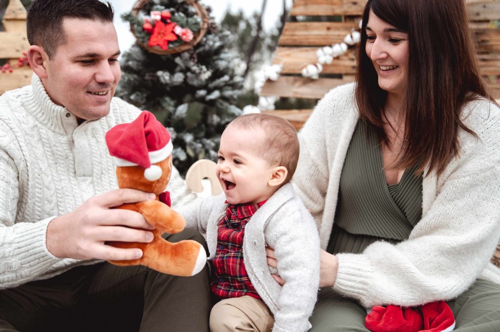 Enfant avec ses parents dans un décor de Noël en bois lors d’une séance photo