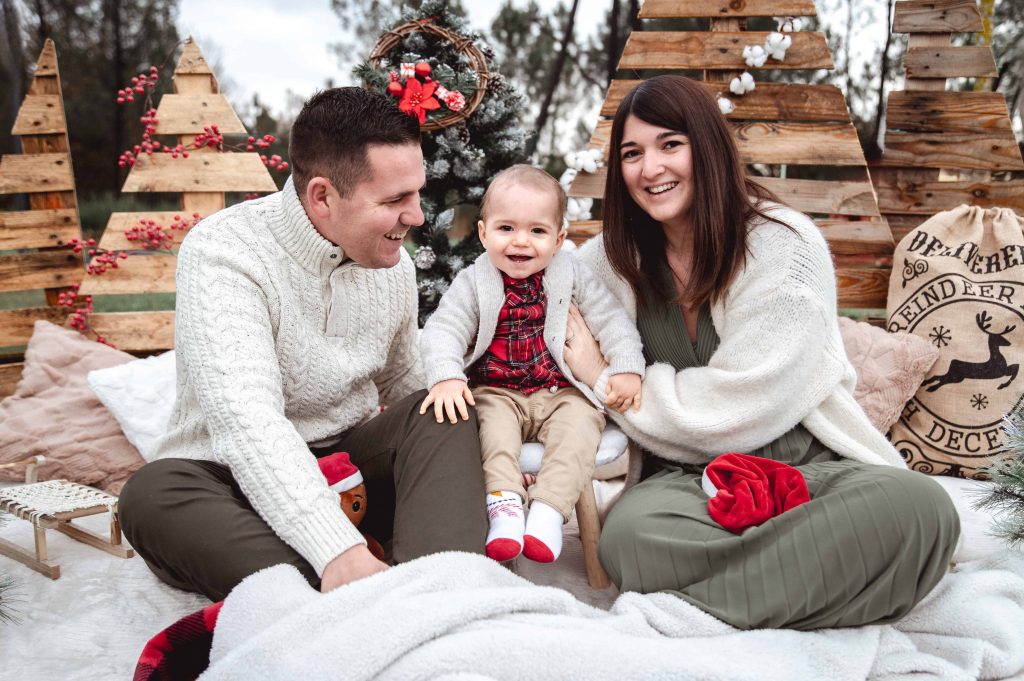 Enfant avec ses parents dans un décor de Noël en bois lors d’une séance photo