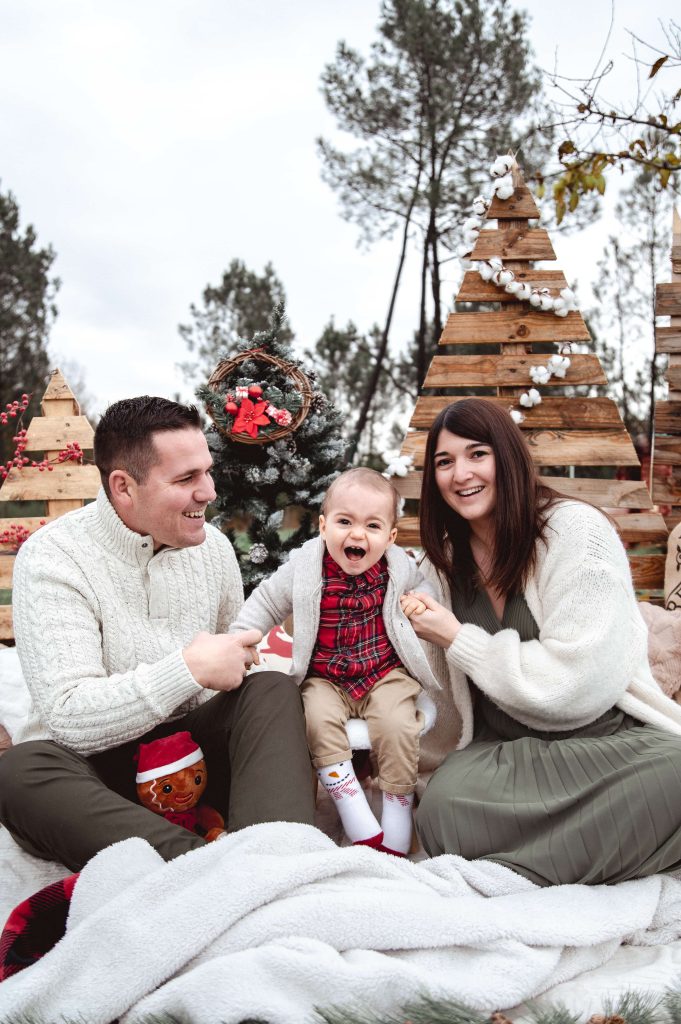 Bébé avec ses parents dans un décor de Noël en bois lors d’une séance photo
