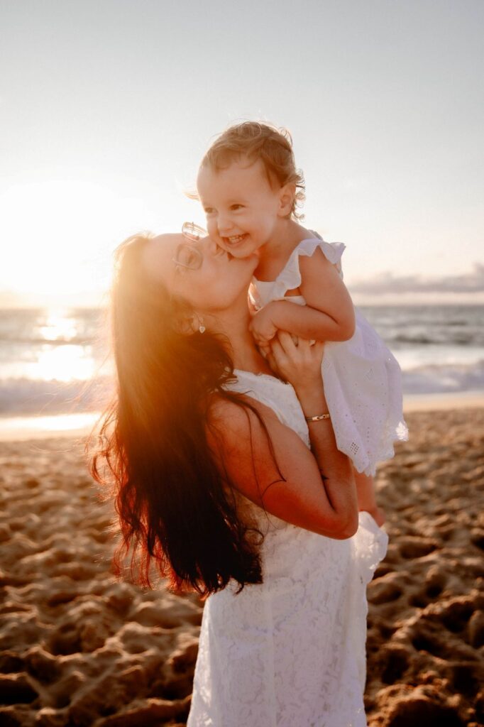 maman qui embrasse son enfant dans la lumière dorée d'une plage à Mimizan
