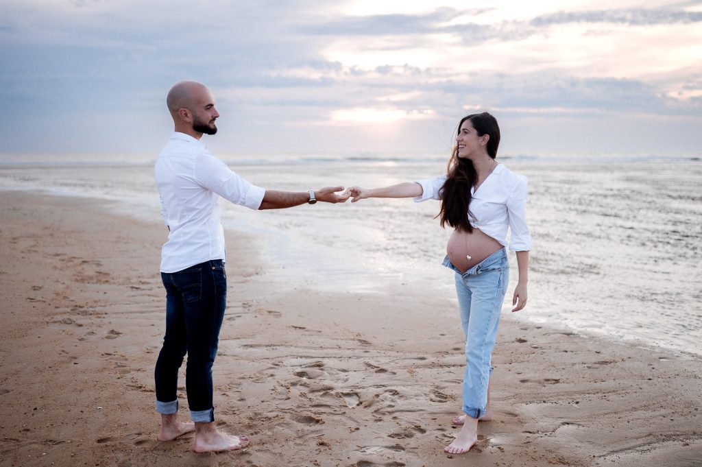 Femme enceinte avec son partenaire dansant sur la plage au coucher du soleil dans les Landes