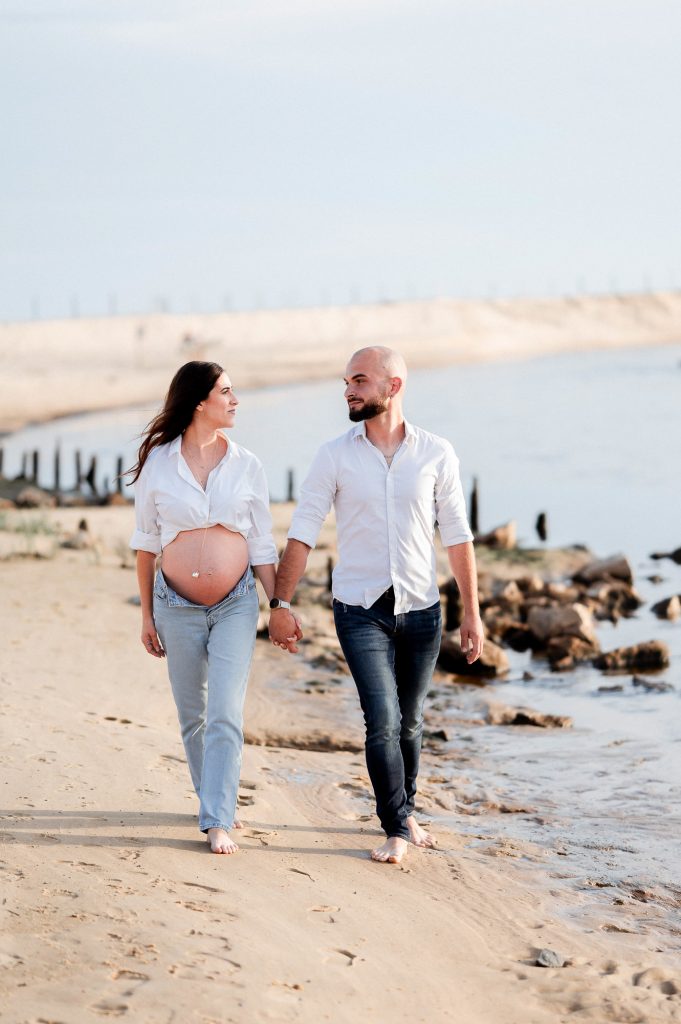 Femme enceinte avec son partenaire marchant sur la plage au coucher du soleil dans les Landes