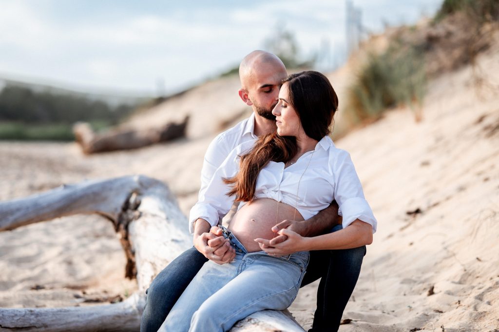 Couple en séance photo grossesse assis sur la plage dans un cadre naturel dans les Landes