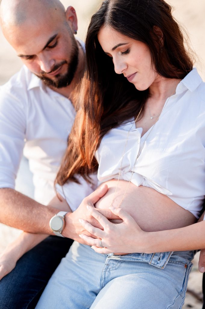 Détail du ventre rond lors d’une séance grossesse en couple sur la plage