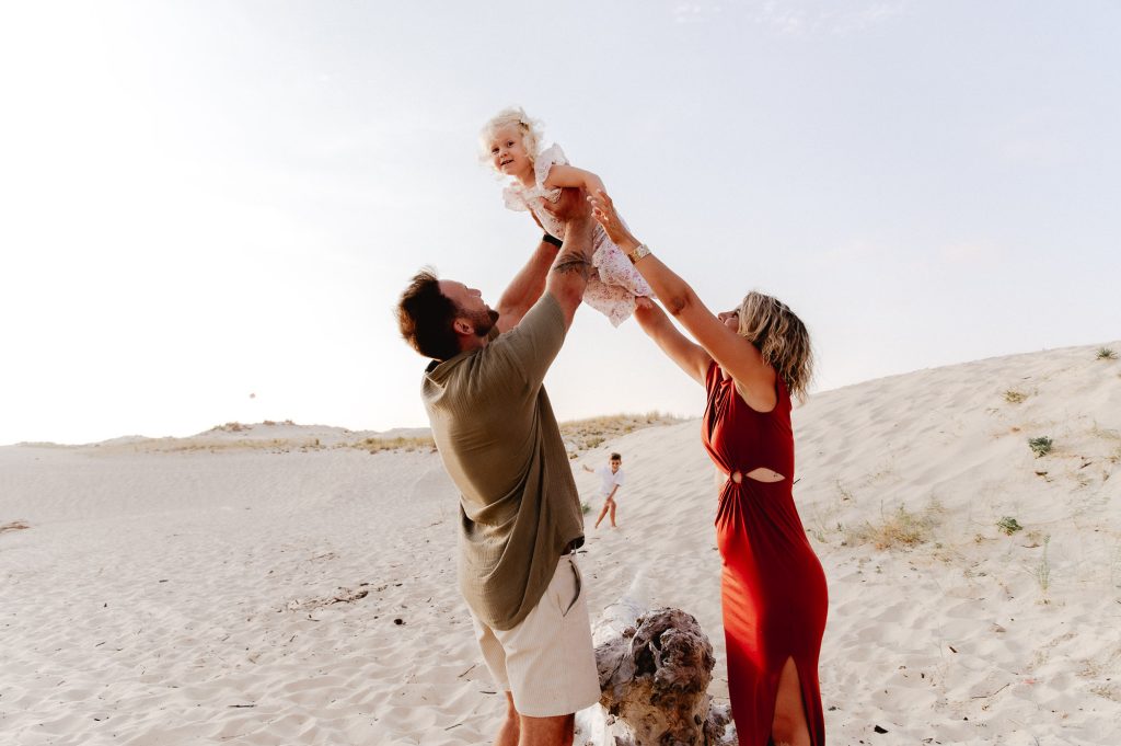 papa et maman tiennent leur fille dans les airs pendant une séance photo à contis plage